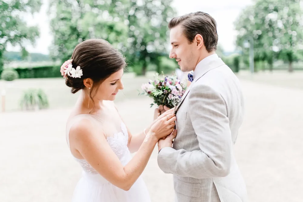 Braut fixiert Blumenanstecker für Bräutigam am Leinenanzug bei First Look zur Hochzeit in Bamberg im Francesco